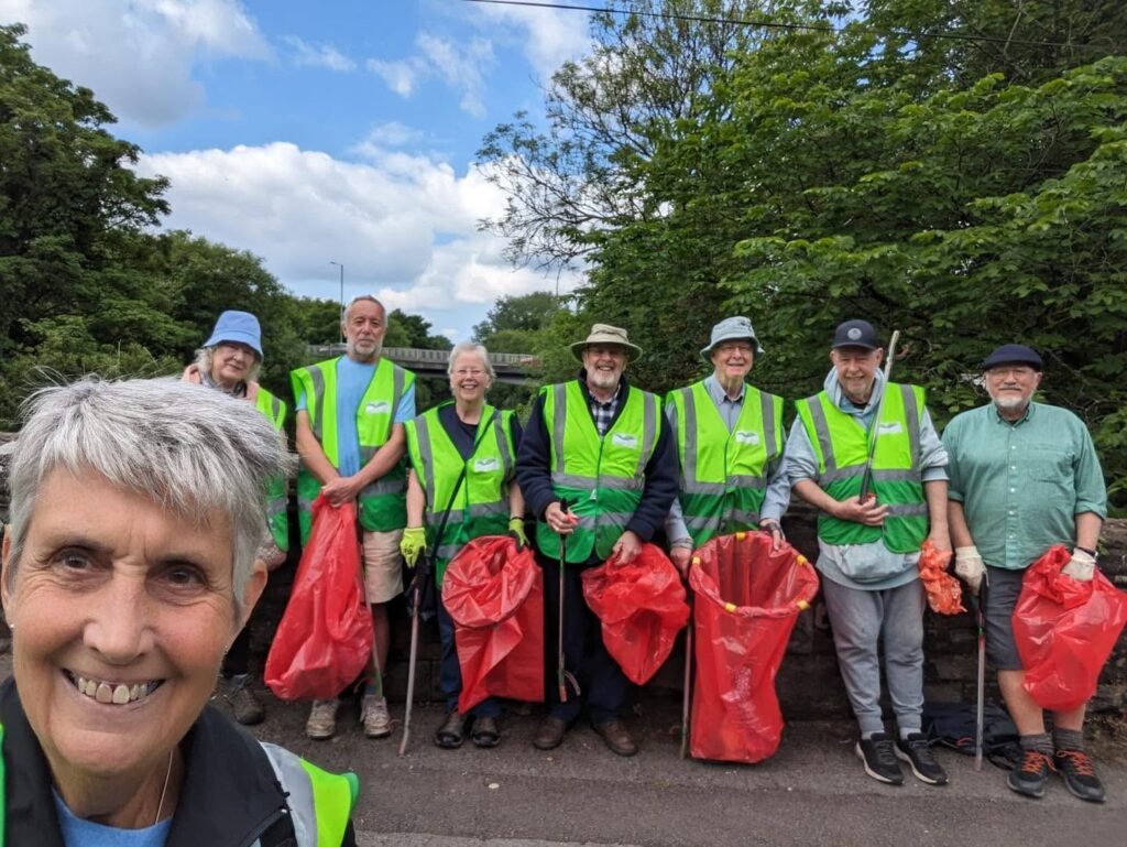 A group selfie of eight litter picking volunteers with red bags on a sunny day