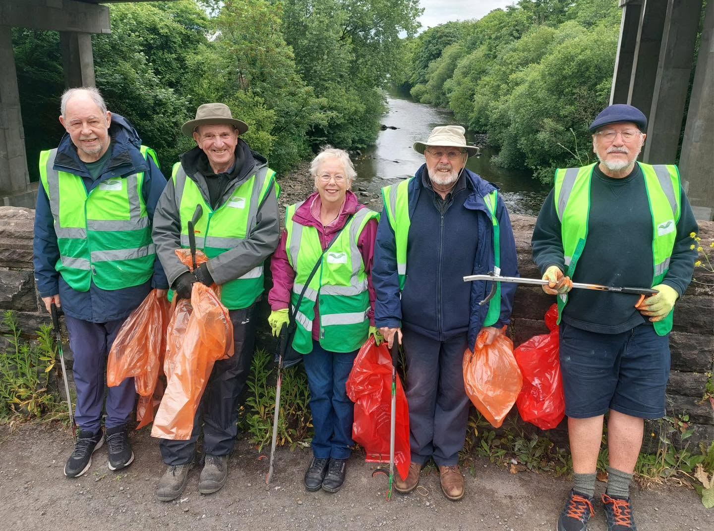 Five volunteers in My Green Valley hi-vis with litter pickers and bags on a river bridge